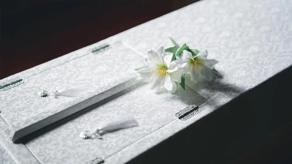 白い棺の上に白い花が置かれた、火葬式のイメージ写真